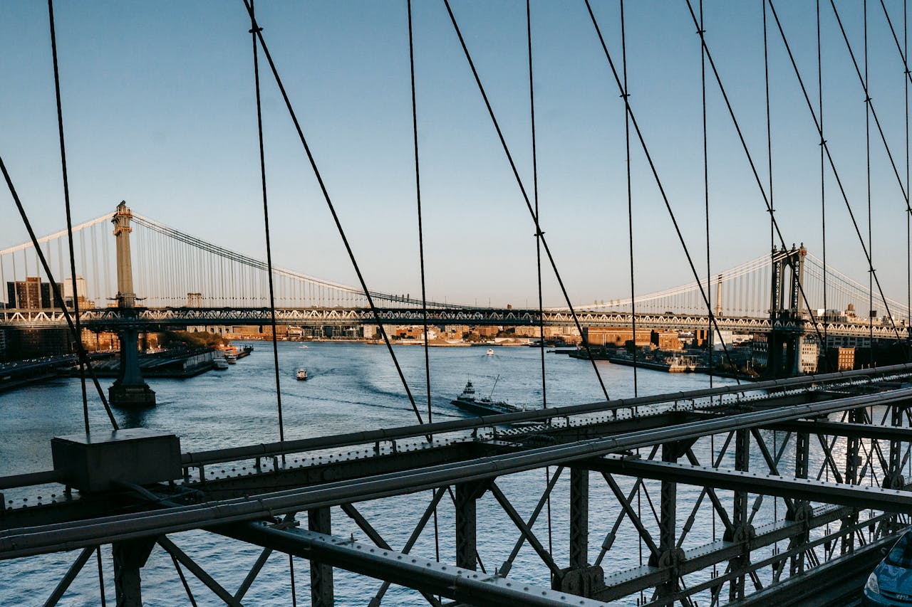 Contemporary suspension bridges over wide river with various vessels under clear blue sky